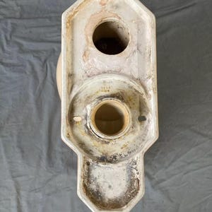 May include: White ceramic toilet bowl base with a round opening and a smaller round opening on the top. The base has a decorative design with a scalloped edge. The base is marked with the text "4444 70000".