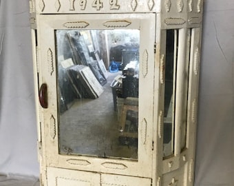 May include: White wooden corner cabinet with a mirror, two drawers, and a small door. The cabinet has a carved design and the number "1942" on the top.