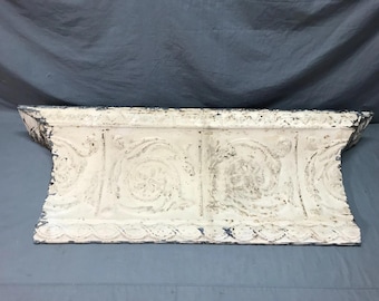 May include: White painted tin ceiling tile with a decorative, embossed pattern. The tile has a scalloped edge and is slightly curved.