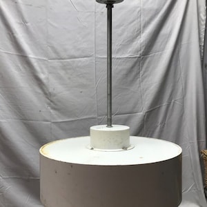May include: A white, round, ceiling light fixture with a metal rod hanging from the ceiling. The light fixture has a simple, modern design.