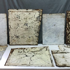 May include: Eight antique tin ceiling tiles with intricate embossed floral patterns. The tiles are white with some rust and wear.