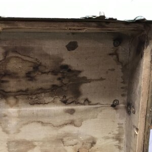 May include: The inside of a vintage green suitcase with a fabric lining. The lining is stained with brown watermarks.