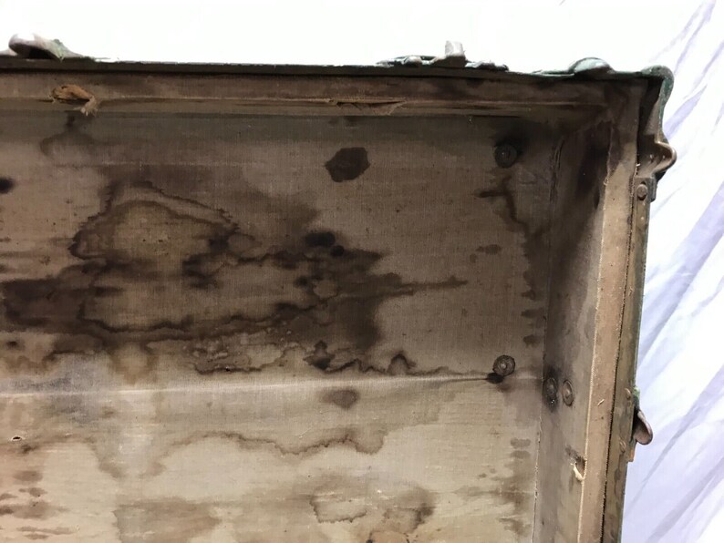 May include: The inside of a vintage green suitcase with a fabric lining. The lining is stained with brown watermarks.