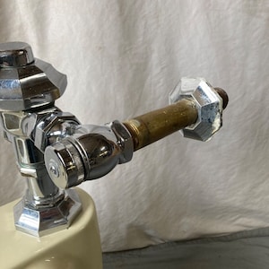 K&ouml;nnte beinhalten: Nahaufnahme einer verchromten Toilettensp&uuml;lkasten-F&uuml;llventile mit einem Messingrohr und einer verchromten Kappe. Das Ventil ist an einem wei&szlig;en Porzellan-Toilettensp&uuml;lkasten befestigt.