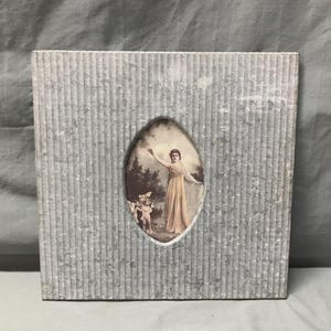 May include: A vintage, square, gray, textured picture frame with a vertical striped pattern. The frame has an oval cutout revealing a sepia-toned image of a woman in a flowing gown with cherubs. The image is a classic, antique style.