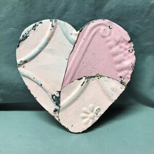 May include: A pink and white heart-shaped wall decor made from repurposed tin tiles. The heart is decorated with a floral pattern and has a distressed finish.