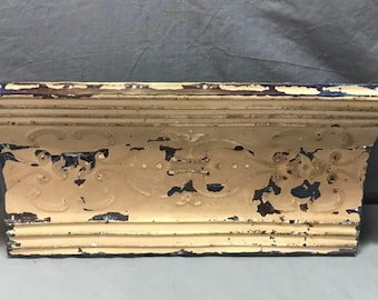 May include: A vintage, cream-colored metal shelf with a decorative floral design. The shelf has a distressed, aged look with some blue paint showing through.