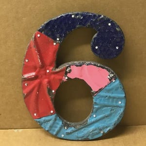 May include: A colorful metal number six with a distressed finish. The number is segmented into sections of red, pink, blue, and navy blue, with white dot accents. This decorative piece is suitable for home decor.