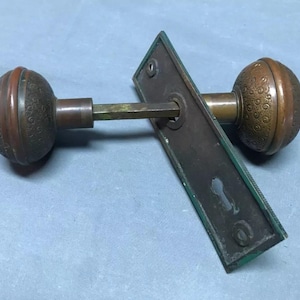 May include: Antique brass door knob set with a decorative pattern. The knob is round and has a keyhole on the back plate.