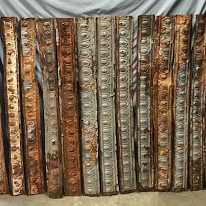 May include: A collection of weathered, rectangular metal panels with a repeating pattern of circles and lines. The panels display a mix of gray, brown, and rust-colored tones, suggesting age and exposure to the elements. The overall aesthetic is rustic and vintage.