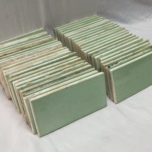May include: Stacks of rectangular, light green tiles with a glossy finish. The tiles are arranged in neat rows, showcasing their uniform shape and color. The edges of the tiles are a lighter shade of green.