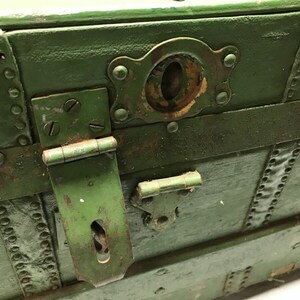 May include: A vintage green wooden trunk with metal accents. The trunk has a hinged lid with a metal latch and a keyhole. The trunk is weathered and shows signs of age.