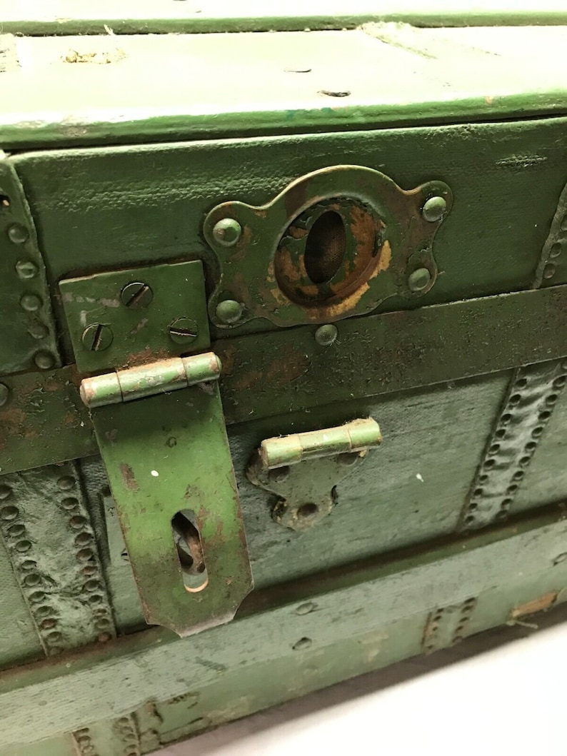 May include: A vintage green wooden trunk with metal accents. The trunk has a hinged lid with a metal latch and a keyhole. The trunk is weathered and shows signs of age.