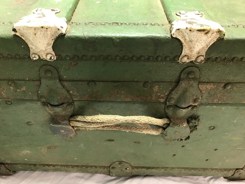 May include: A vintage green metal trunk with rope handles and white metal clasps. The trunk has a worn, distressed look.