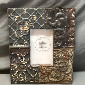 May include: A rectangular photo frame with a distressed, vintage appearance. The frame is composed of several textured panels in shades of gray, brown, and gold. The center holds a white insert with the text "NEW YORK SALVAGE".