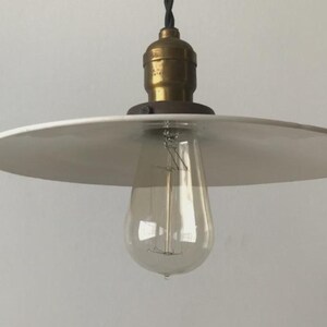 May include: A vintage-style pendant light fixture with a white, circular shade and a clear, teardrop-shaped light bulb. The fixture has a brass-colored socket and a black cord. The light is suspended from the ceiling, creating a warm, inviting ambiance.
