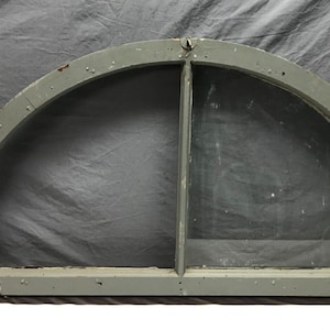 May include: A large, arched window frame made of wood, painted a light gray color. The frame is divided into two sections by a vertical piece of wood. The window is missing the glass panes.