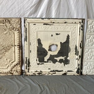 May include: Three vintage tin ceiling tiles with a white and gray paint finish. The tiles have a decorative embossed pattern and are in good condition.