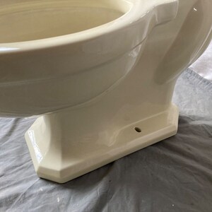 May include: A cream-colored toilet bowl with a rounded, oval-shaped bowl and a pedestal base. The toilet bowl is made of ceramic and has a smooth, glossy finish.