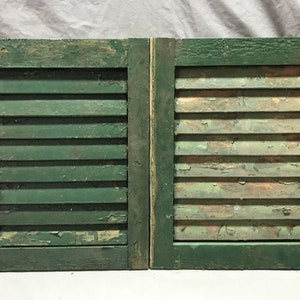 May include: A pair of antique green wooden shutters with a distressed finish. The shutters are closed and have a simple design with horizontal slats.