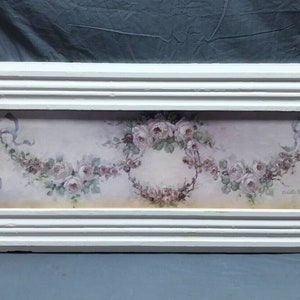 May include: A white framed picture with a floral design featuring pink roses and blue ribbons. The picture is on a light gray background. The artist's signature is visible in the bottom right corner.