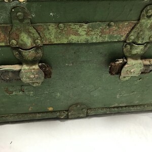 May include: A vintage green metal trunk with two metal clasps and leather straps. The trunk has a worn and weathered appearance, with rust and paint chips visible.