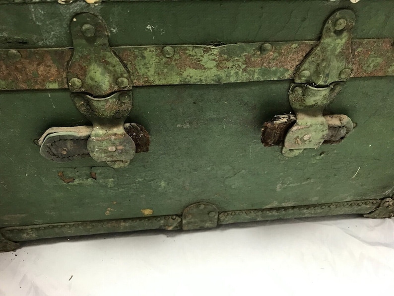 May include: A vintage green metal trunk with two metal clasps and leather straps. The trunk has a worn and weathered appearance, with rust and paint chips visible.