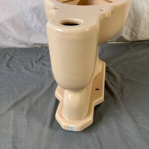 May include: A cream-colored toilet bowl with a Kohler USA label on the bottom. The bowl is made of ceramic and has a smooth, glossy finish.