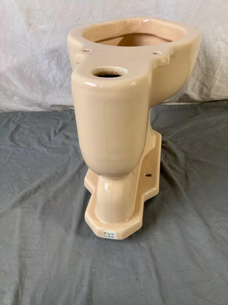 May include: A cream-colored toilet bowl with a Kohler USA label on the bottom. The bowl is made of ceramic and has a smooth, glossy finish.