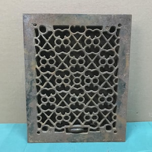 May include: A rectangular cast iron floor register featuring a dark, weathered brown finish and an intricate, repeating lattice pattern of interconnected geometric shapes. The metal grate includes four corner screw holes and a small lever at the bottom.