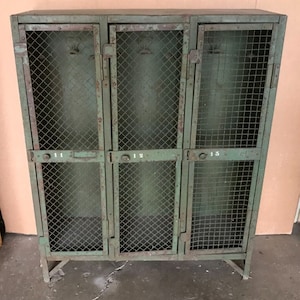 May include: A green metal locker with three compartments, each with a wire mesh door. The doors are labeled with the numbers 11, 12, and 13.