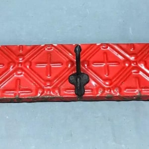 May include: A red tin tile wall mounted coat rack with three black metal hooks.