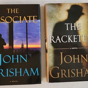 May include: Two paperback books by John Grisham. The book on the left is titled "The Associate" and features a cityscape at sunset. The book on the right is titled "The Racketeer" and features a shadowy figure in the background.
