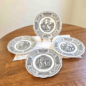 May include: Four round ceramic plates featuring black and white illustrations of figures in historical clothing. Each plate has a decorative border with intricate patterns. The central images depict various scenes with French text printed below them.