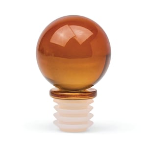 May include: A bottle stopper featuring a smooth, spherical amber-coloured glass top with a reflective surface. The base consists of a tiered, semi-translucent white silicone plug with four distinct ridges designed for a secure fit in a bottle neck.
