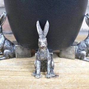 May include: Three silver rabbit figurines are used as feet for a black planter. The rabbits are in a sitting position with their ears perked up.