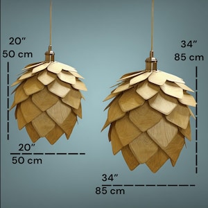 Puede incluir: Dos l&aacute;mparas colgantes de madera, una de 50 cm de ancho y la otra de 85 cm. Cada l&aacute;mpara tiene un dise&ntilde;o en capas, en forma de p&eacute;talos, en tonos marr&oacute;n claro y est&aacute; suspendida por un fino cable dorado.