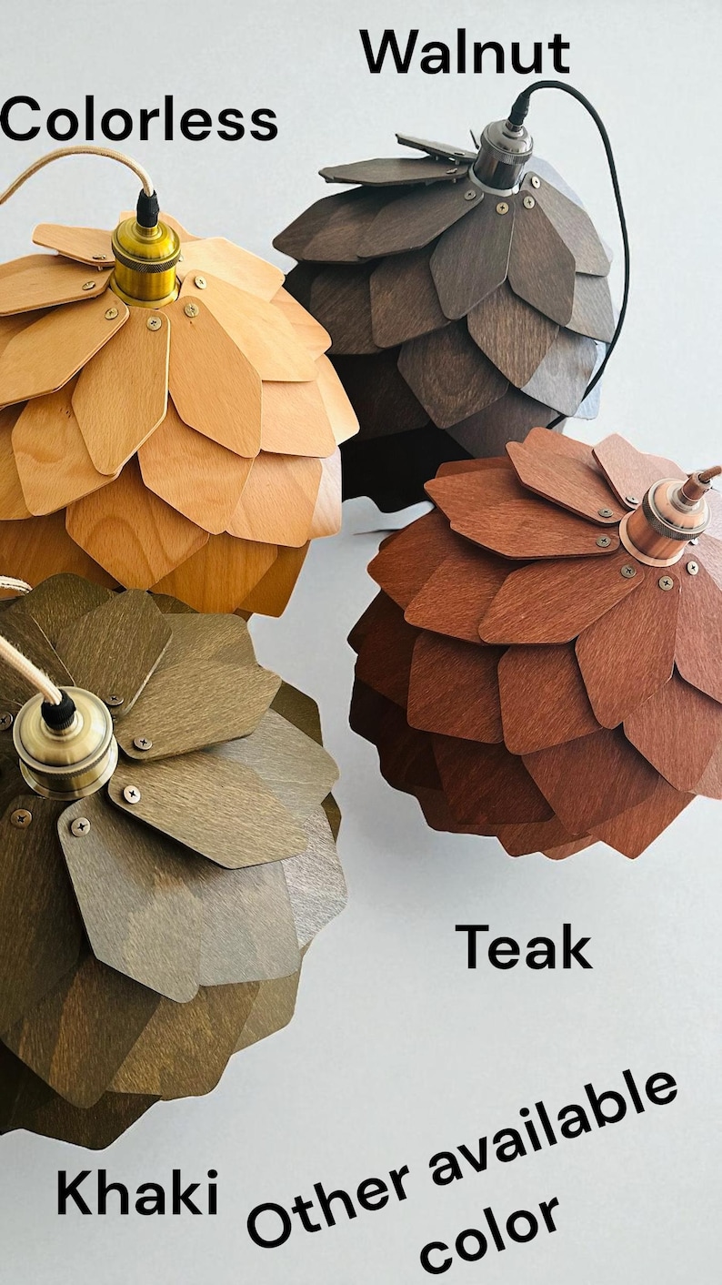 Puede incluir: Cuatro l&aacute;mparas colgantes de madera en varios colores: incoloro, nogal, teca y caqui. Cada l&aacute;mpara tiene un dise&ntilde;o &uacute;nico en forma de p&eacute;talo y un accesorio de lat&oacute;n o cobre. Tambi&eacute;n se ve el texto "Otro color disponible".