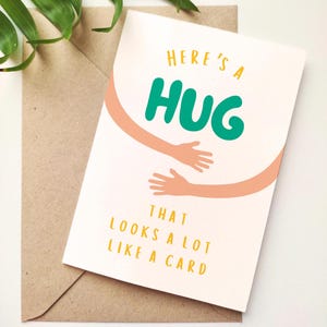 May include: A greeting card with the words "Here's a HUG that looks a lot like a card" in teal and yellow. The card features an illustration of arms in a hugging gesture. The card is on top of a brown envelope.