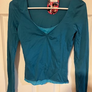 May include: A teal long-sleeved shirt with a scoop neck and a sheer overlay. The shirt has a gathered detail at the neckline. The tag on the shirt reads "Kohl's $24.02".