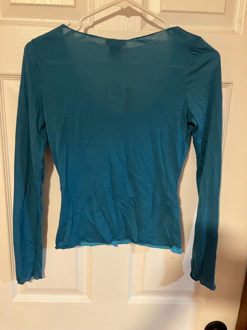 May include: A teal blue long-sleeved shirt with a scoop neck and a slightly ruffled hem.