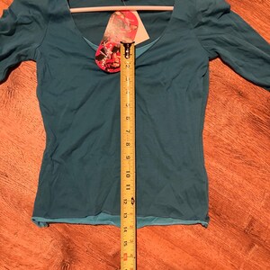 May include: A teal blue, long-sleeved shirt with a scoop neck. The shirt is on a hanger and has a tag that says "Energie" on it.