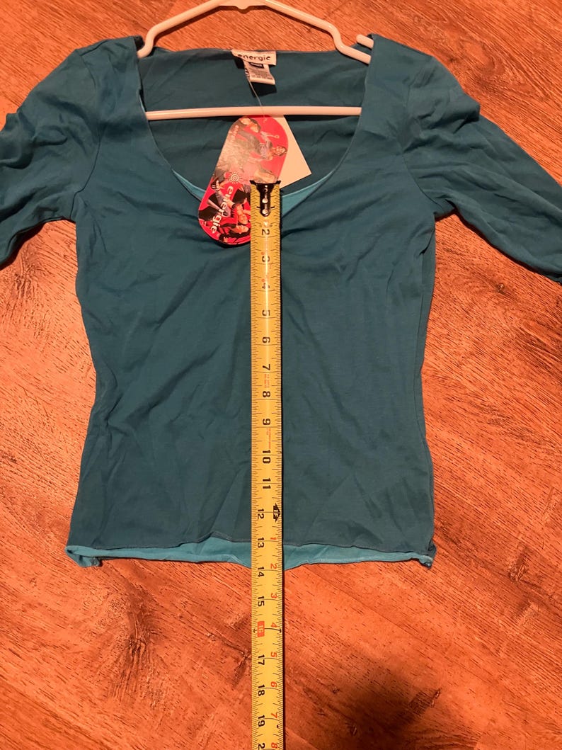 May include: A teal blue, long-sleeved shirt with a scoop neck. The shirt is on a hanger and has a tag that says "Energie" on it.