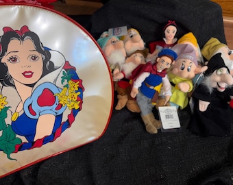 May include: A collection of Snow White and the Seven Dwarfs merchandise. Includes a white and red Snow White lunchbox with a cartoon image of Snow White, and plush dolls of Snow White, the Prince, and the Seven Dwarfs.