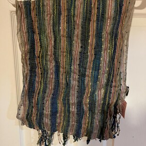 K&ouml;nnte beinhalten: Ein gestreifter Schal mit Fransen. Der Schal ist aus einem durchsichtigen Stoff gefertigt und hat einen metallischen Glanz. Die Farben der Streifen sind Blau, Gr&uuml;n, Rot und Gold.