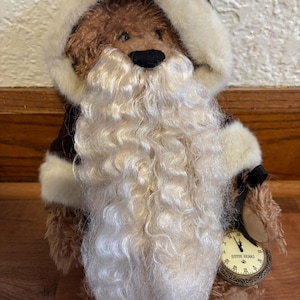 May include: A Boyd's Bears plush bear dressed as Santa Claus, with a white fur-like beard and a matching hood. The bear holds a pocket watch with the words "Boyds Bears" on the face. The bear is wearing a brown coat with white trim.