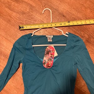 May include: Teal long-sleeve shirt with a scoop neck and a small tag that says "Energie" on it.