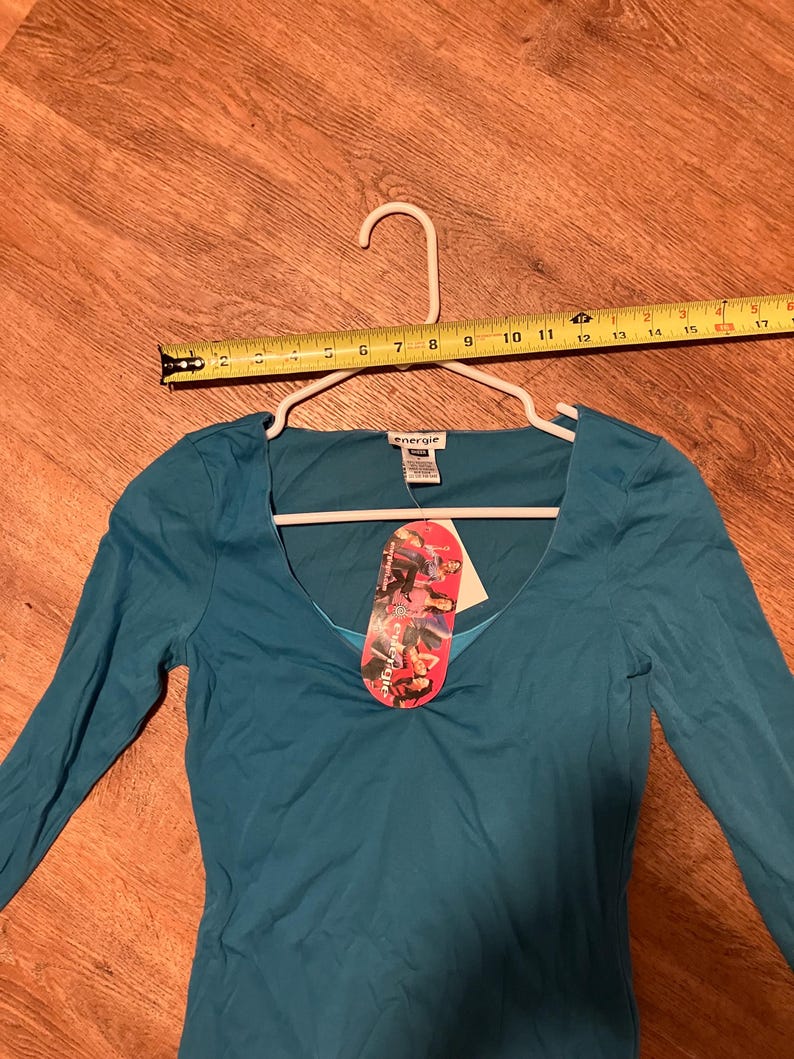 May include: Teal long-sleeve shirt with a scoop neck and a small tag that says "Energie" on it.