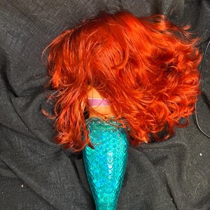 May include: A mermaid doll with long, curly red hair and a turquoise tail with a sparkly finish.