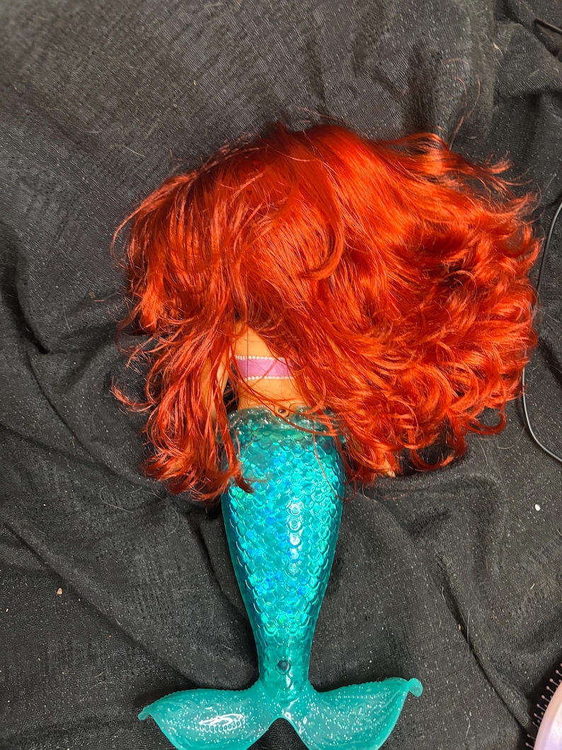 May include: A mermaid doll with long, curly red hair and a turquoise tail with a sparkly finish.